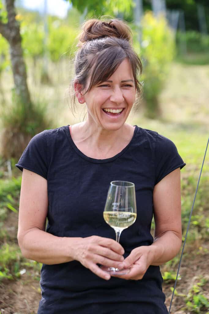 Weingut vulgo Ritter, Frau mit Glas Weißwein, winzerliche Atmosphäre, Weinverkostung im Weinberg, Genusserlebnis, Nachhaltiger Weinbau, Weinkultur, ländliche Weingut-Umgebung, Weinliebhaber, Natur und Weingut.